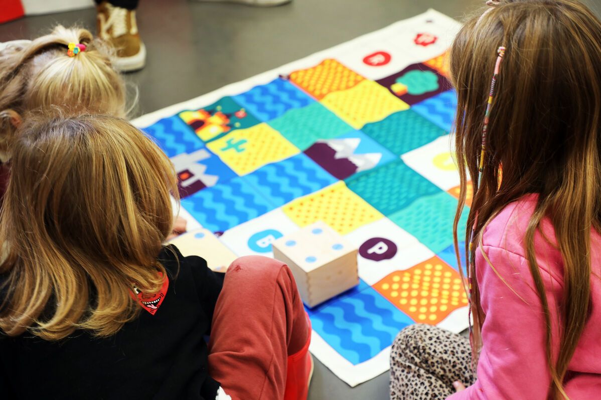 Un groupe d'enfants qui apprend à programmer avec une commande numérique et un tapis où un petit cube robot avance en fonction de la programmation établie